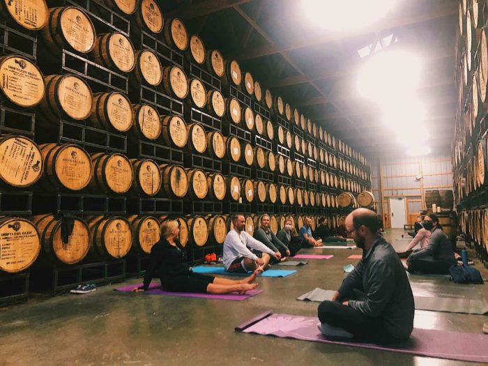 Yoga & Whiskey attendees stretch on their yoga mats in front of barrels of aging whiskey.