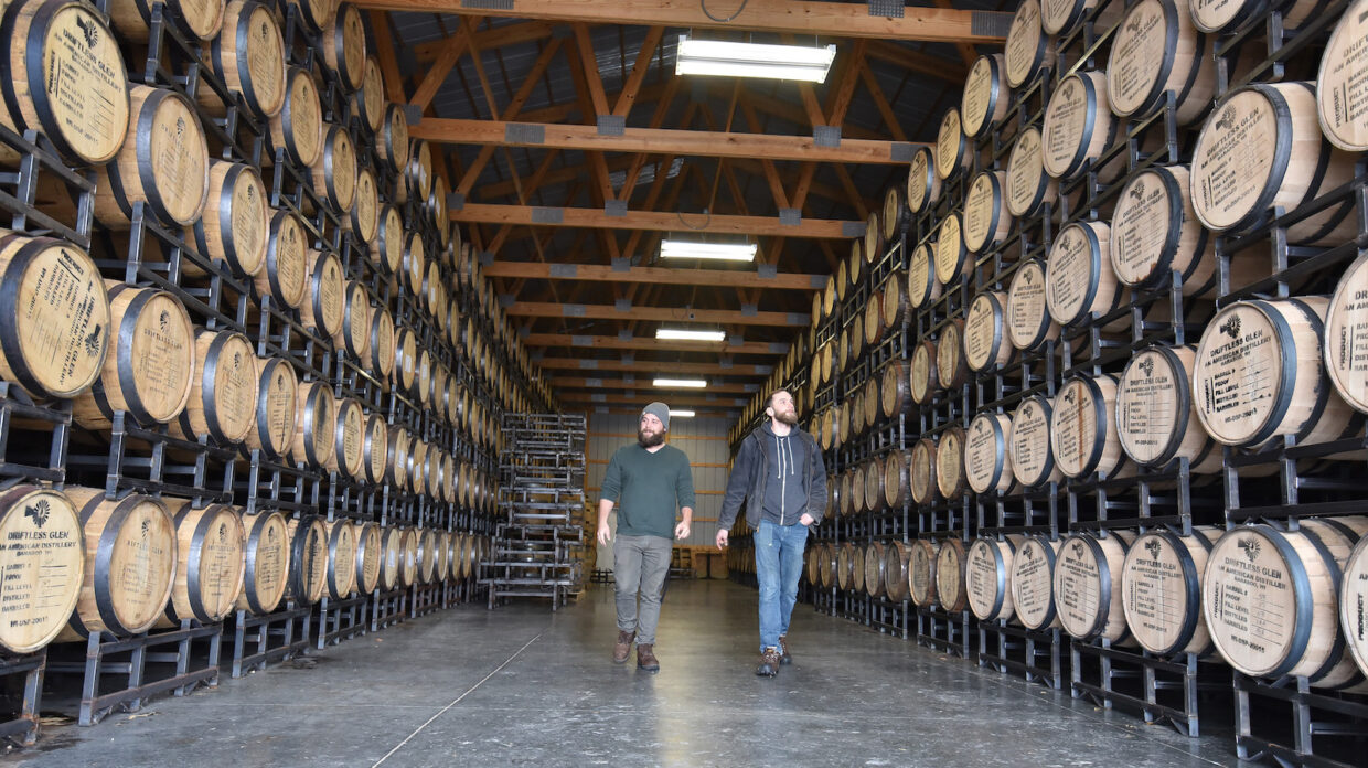 Distillers Nathan and Max at Driftless Glen walk through the rackhouse, surrounded by barrels of aging whiskey. The image was featured on the front of the Whiskey Advocate article. 
